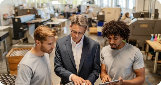 Groupe de 3 personnes regardant une tablette dans un environnement de travail, avec des colis emballés